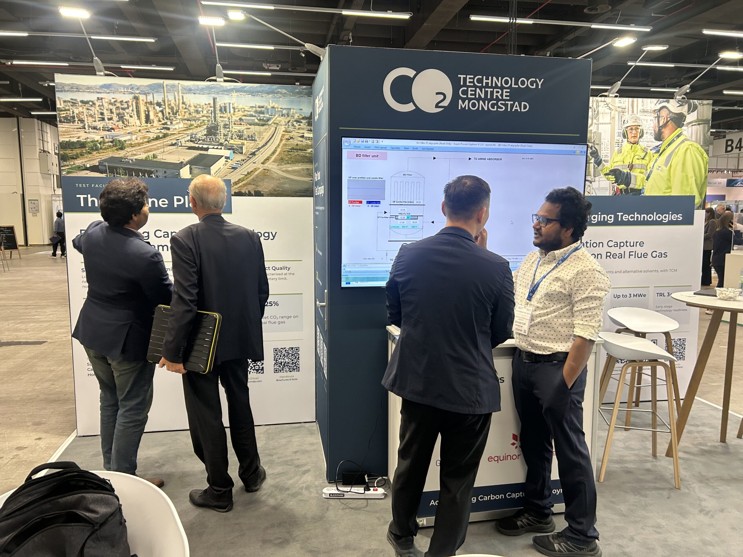 TCM`s stand in Hamburg. Managing Director Ismail Shah (left) and CO<sub>2</sub> Capture Expert Koteswara Rao Putta explain the testing opportunities at the Mongstad facility to two exhibition visitors.